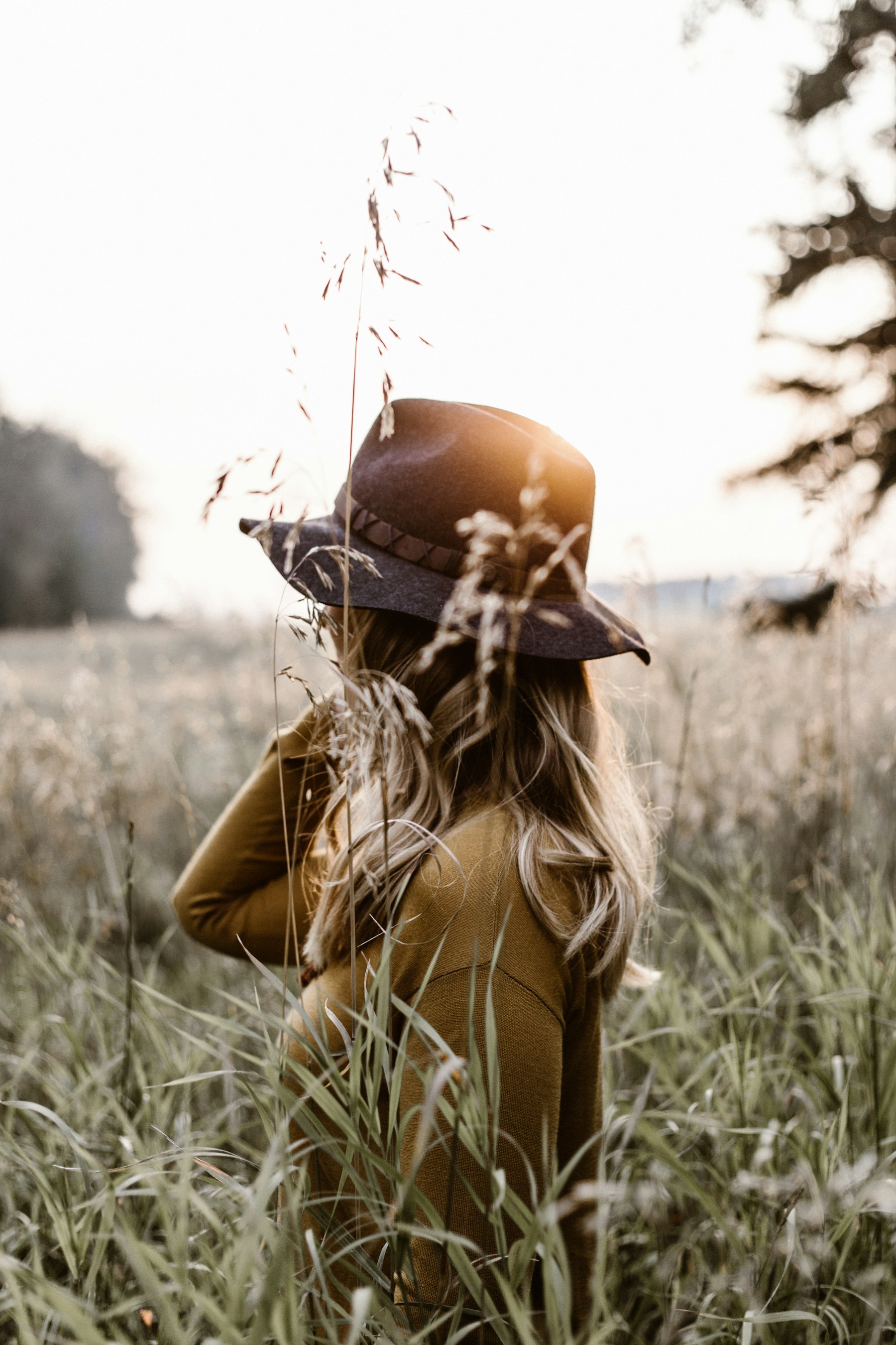 Woman in a mustard knit and felt hat standing in a golden autumn field at sunset