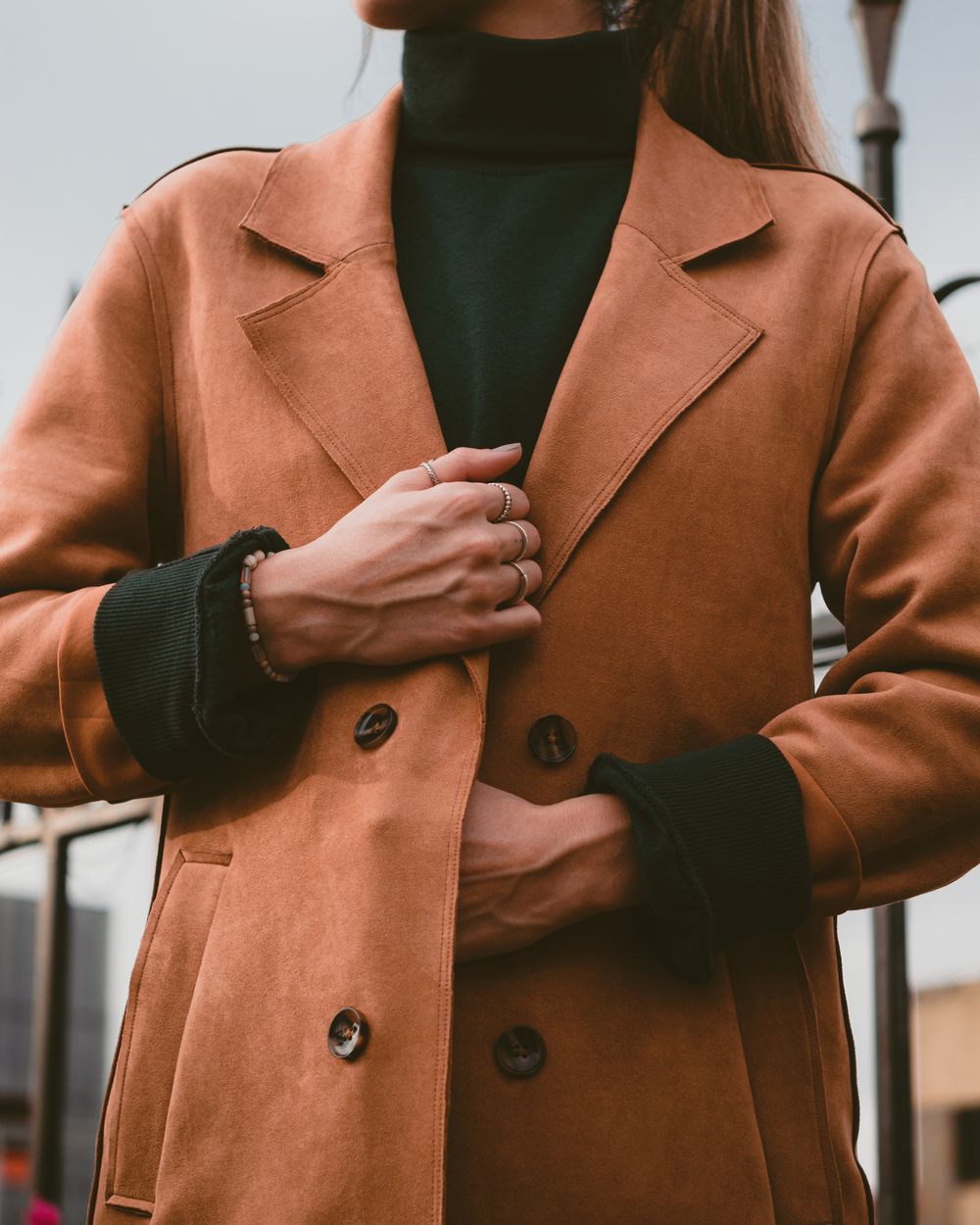 Woman in a warm brown double breasted coat over a green roll neck
