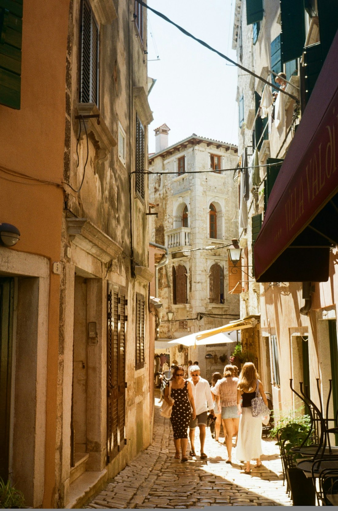 Sunlit old town street in Italy with people walking past warm pastel buildings