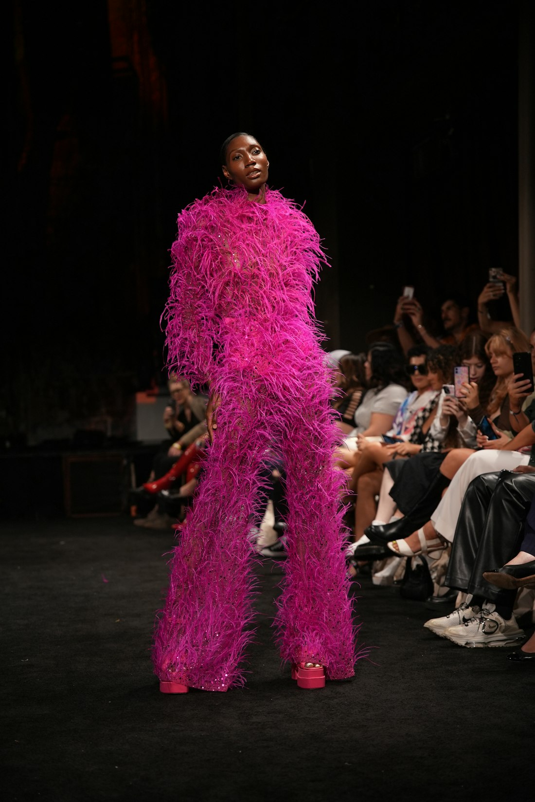 Model on a runway in a bold fuchsia feathered outfit