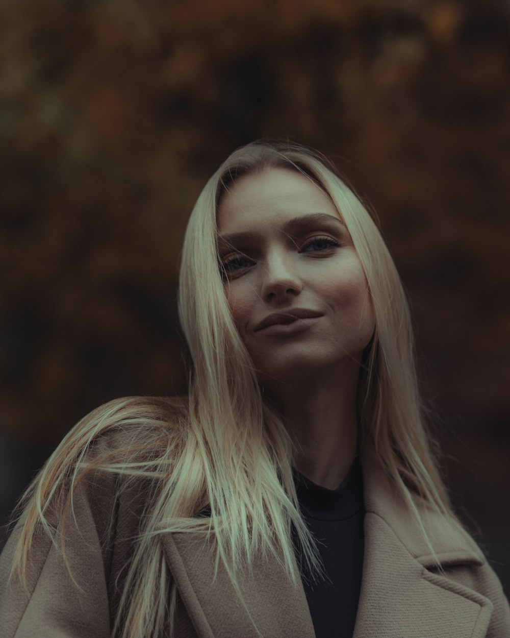 Blonde woman in a soft beige coat against a warm autumn background